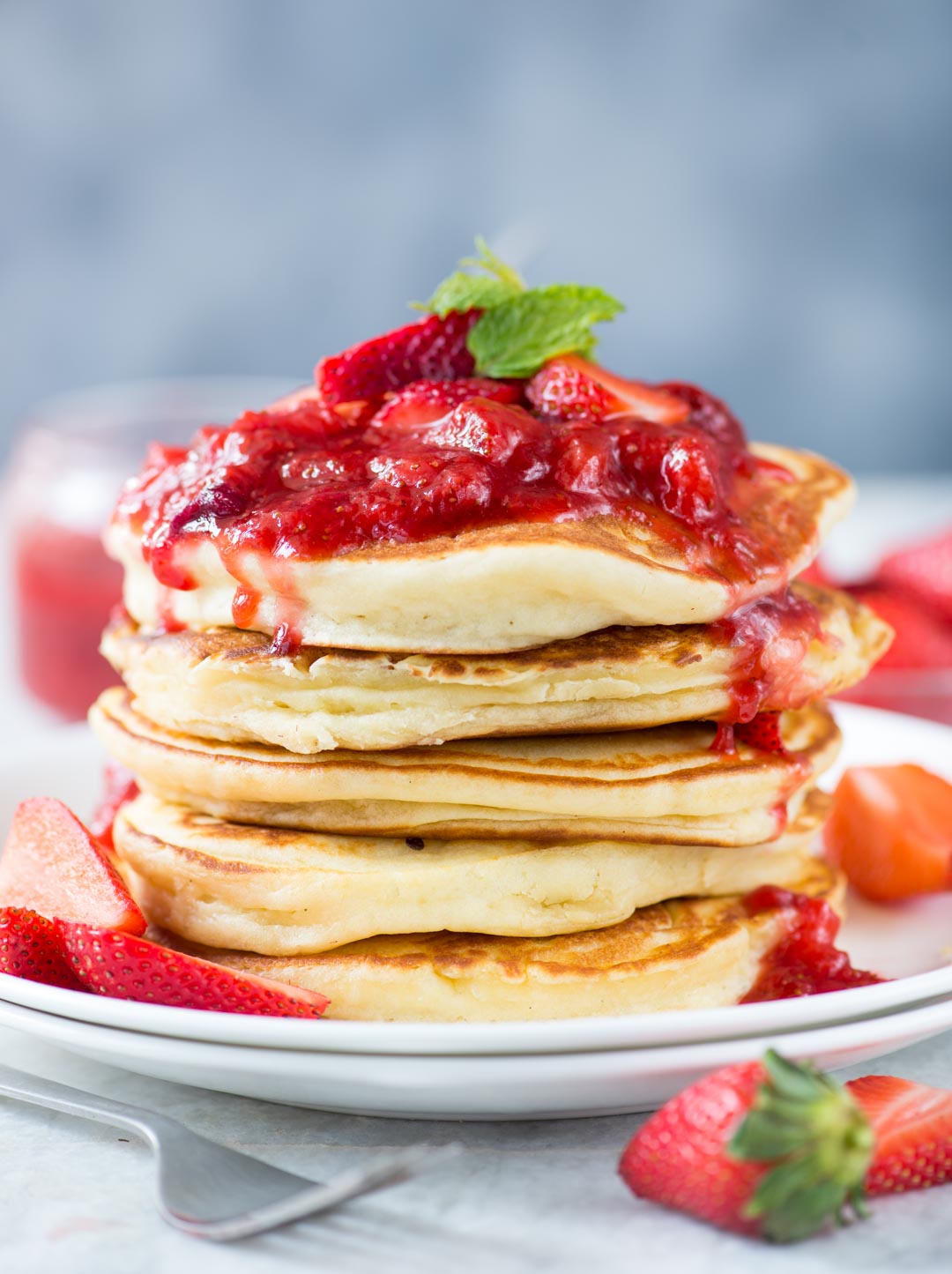 A stack of pancakes made with ricotta cheese and beautiful strawberry sauce on top of it.