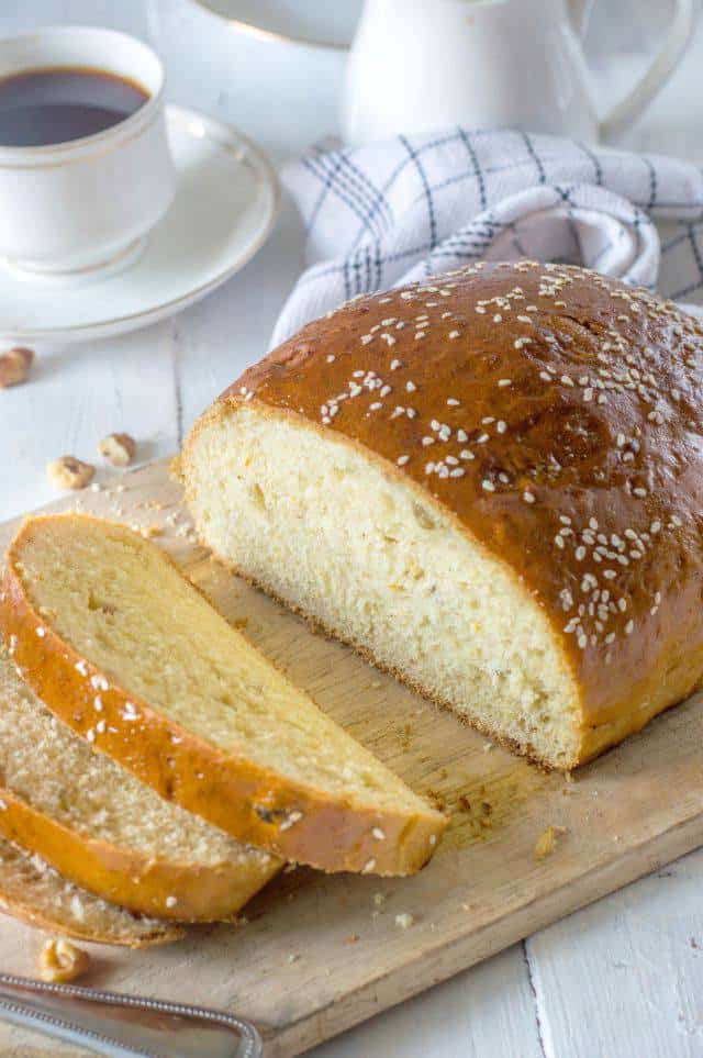 Picture of a loaf of artos greek celebration bread along with few slices on a chop board.