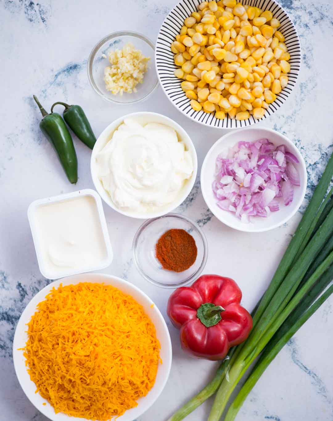 Ingredients shown to make corn dip - Corn, cheese, sour cream, bell pepper, onion, green onion, jalapeno, hot sauce
