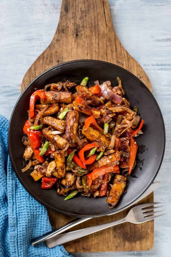 Tofu crisp pan fried with chinese garlic sauce on a black plate placed on a wooden board.