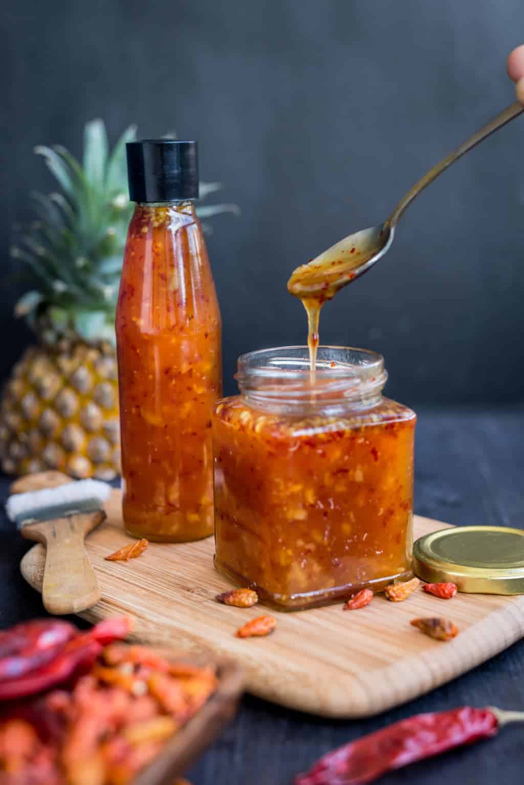 Spoonful of sweet and hot pineapple sauce filling up a jar.
