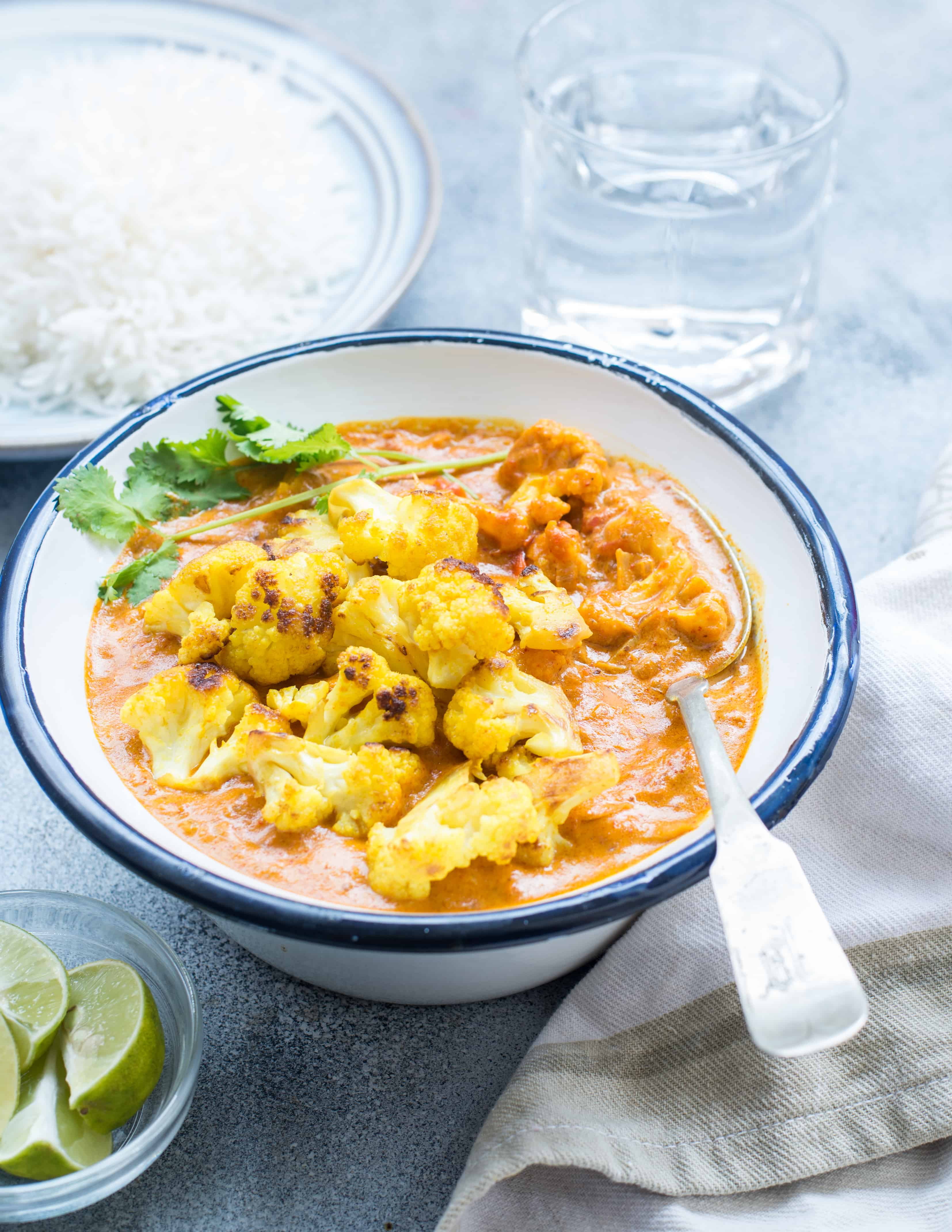 Roasted cauliflower florets on top of curry gravy in a white bowl topped with fresh cilantro.