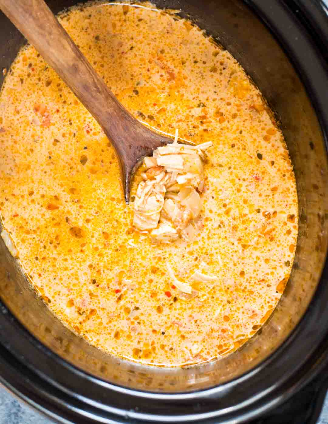 Creamy Mexican Chicken Soup shown made in a crockpot with a ladle picking up pieces of chicken from a creamy soup.
