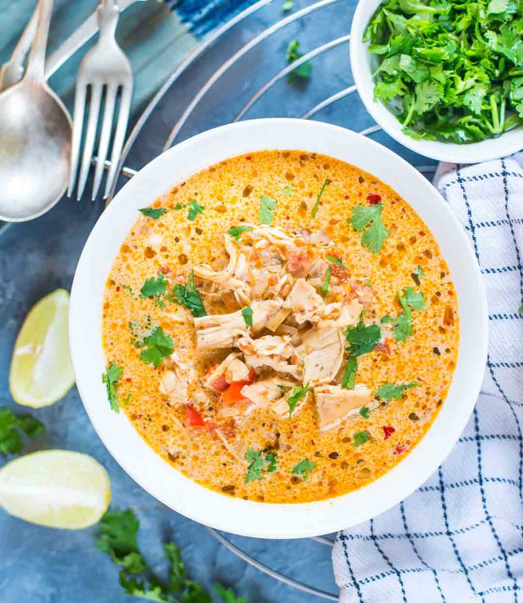 Mexican Chicken Soup served in a bowl with lemon slices and a bowl of cilantro leaves plated beside it.