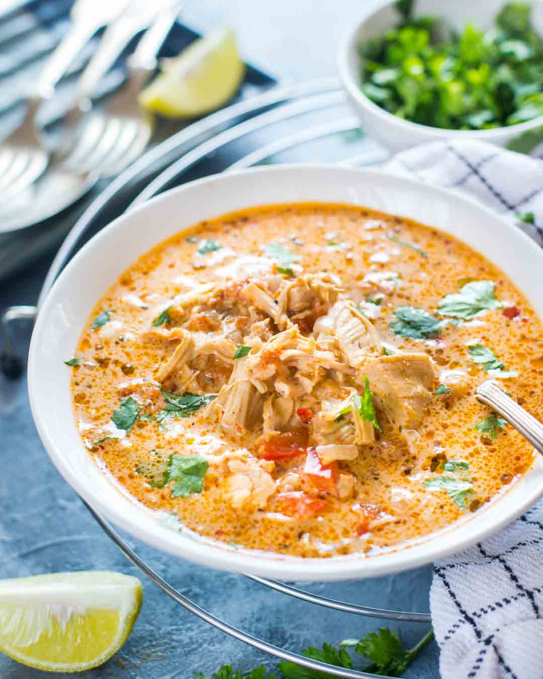 Close-up of flavorful Mexican Chicken Soup served in a bowl with chicken pieces, cilantro, bell pepper and creamy soup shown on the surface with a spoon.