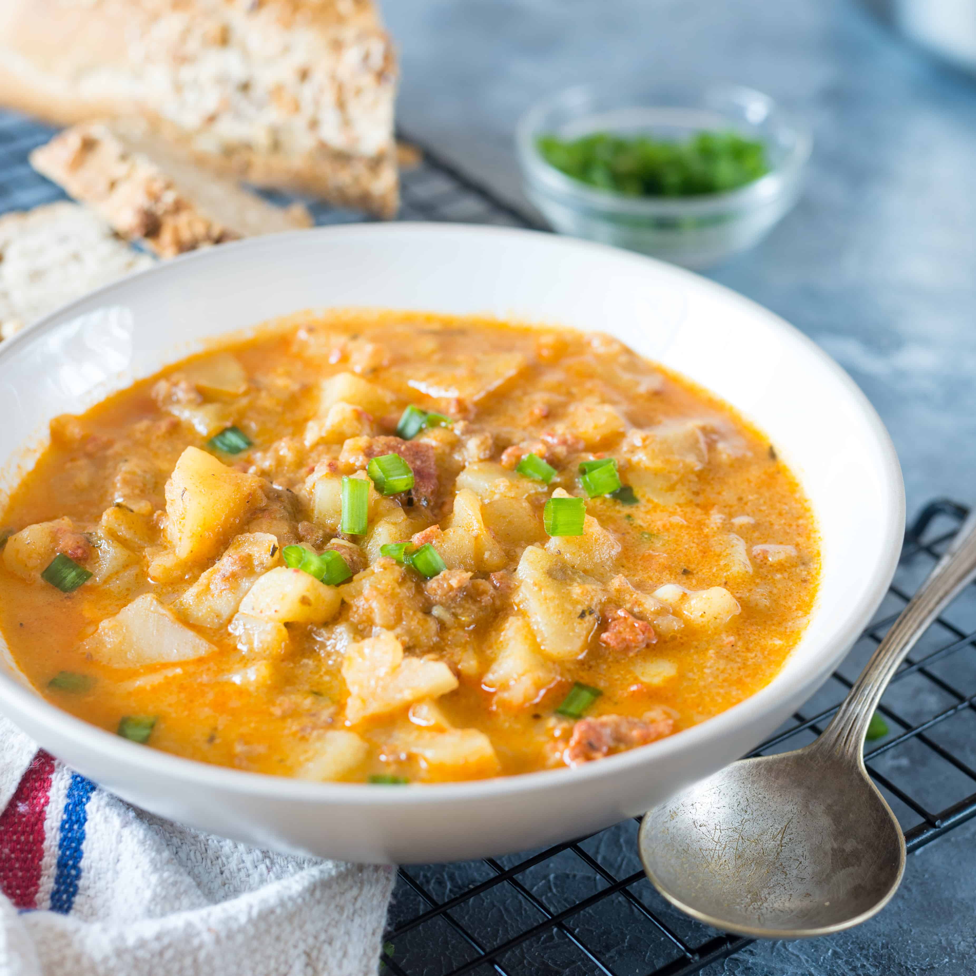 Creamy Chorizo Potato Soup is a rich, delicious and soul-satisfying meal served in a white bowl, alongside crusty bread.