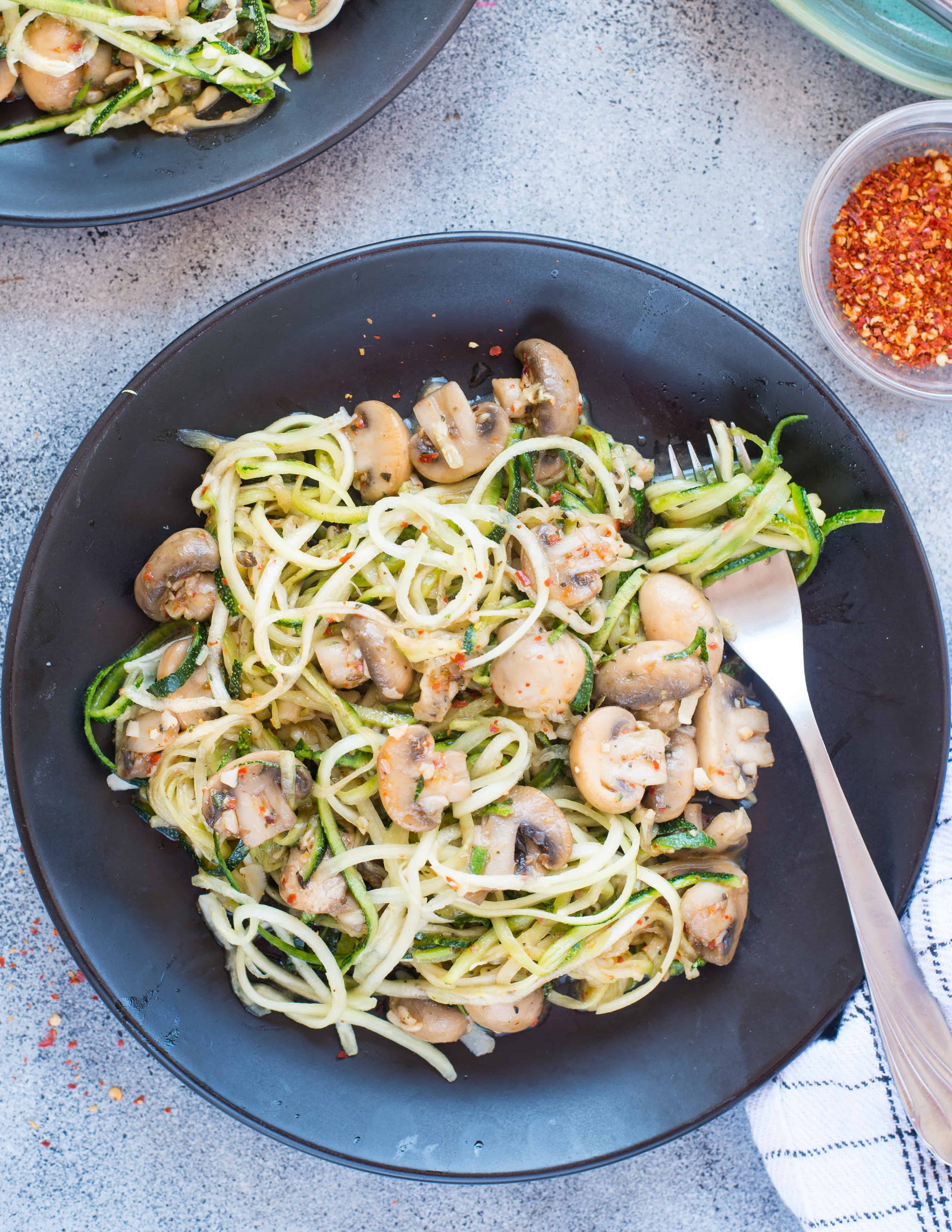 Garlic Parmesan Mushroom Zoodles served on a black bowl and with fork.