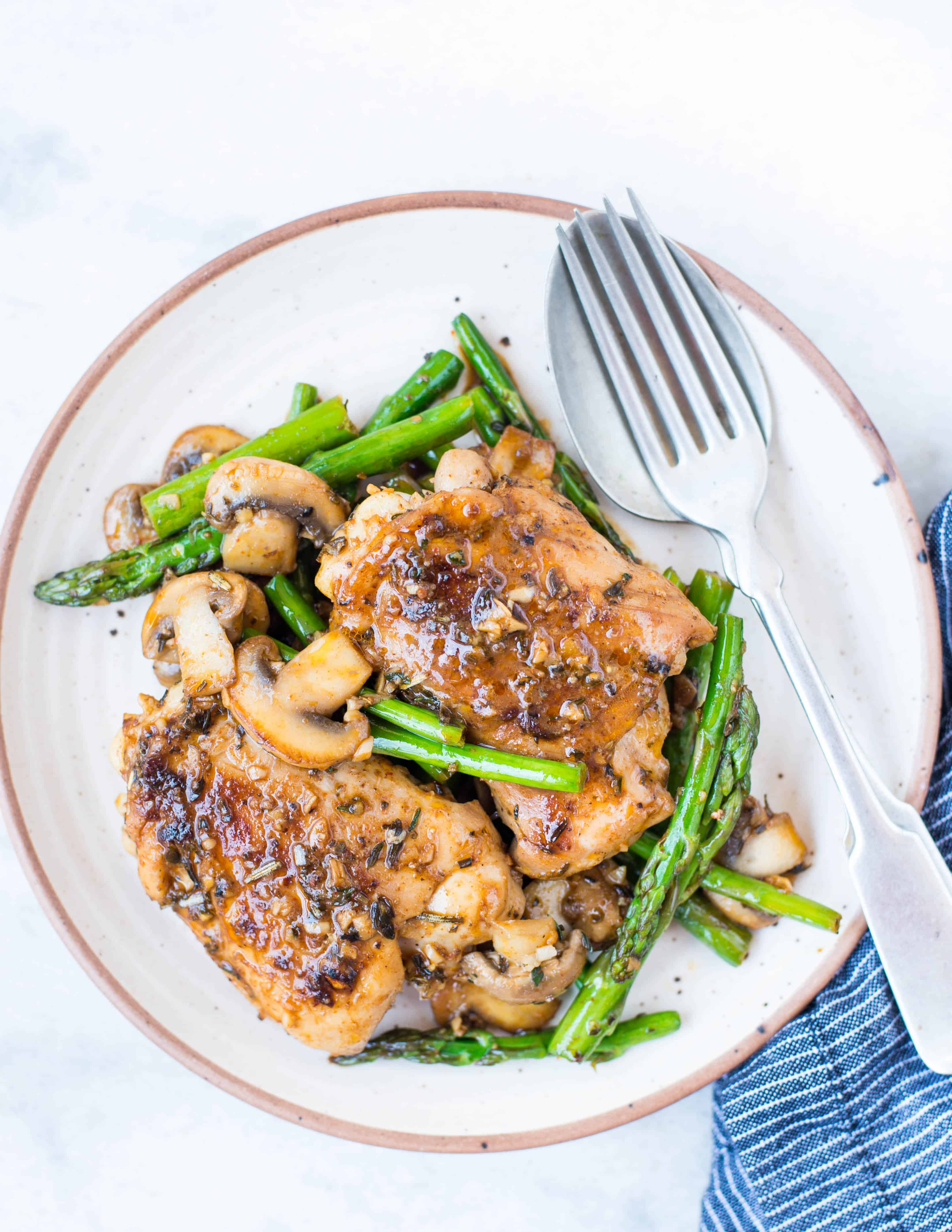 Chicken with lemon butter sauce and asparagus and mushroom served with spoon and fork.