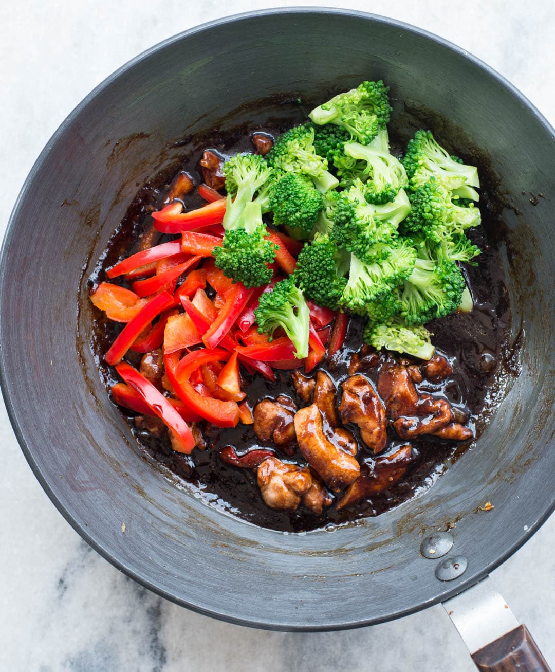 Vegetables like chili-peppers and broccoli added to chicken cooked in asian stir fry sauce in asian wok.