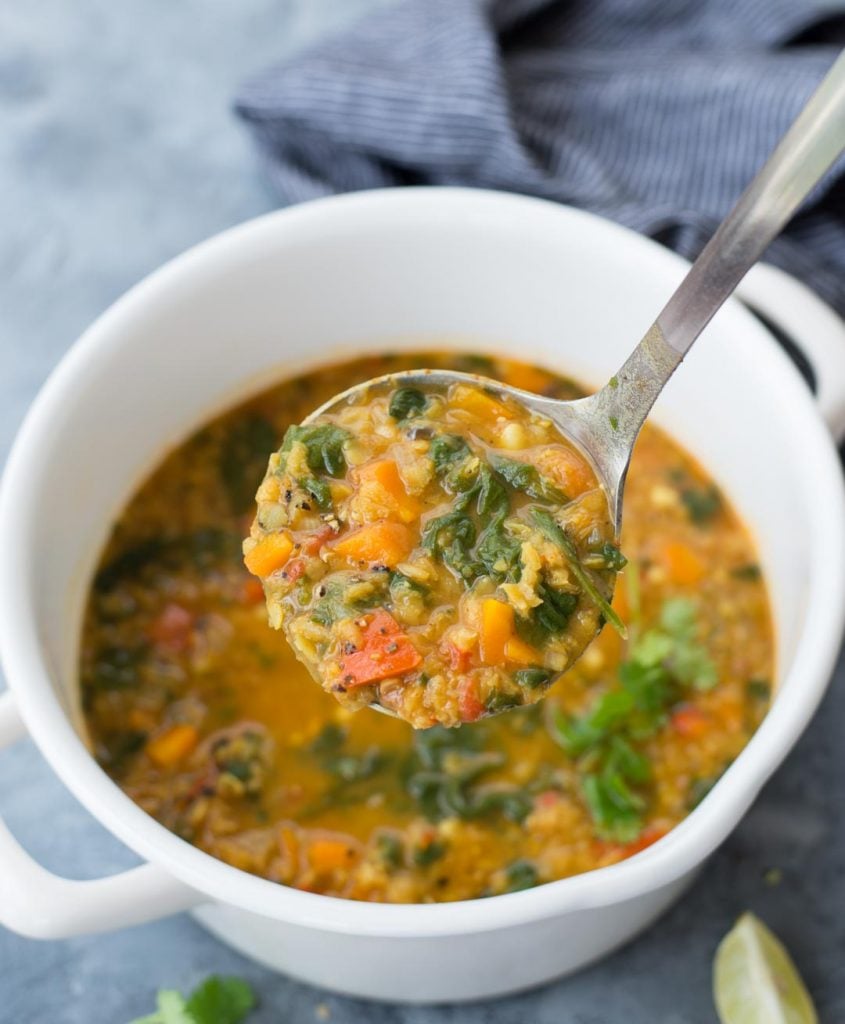 Ladle of red lentil soup made of spinach, lentils, carrots and spiced made in white dutch oven.