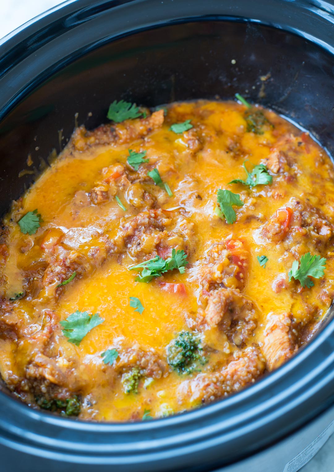 Melted cheese on top of a chicken broccoli quinoa casserole, made in a slow cooker.