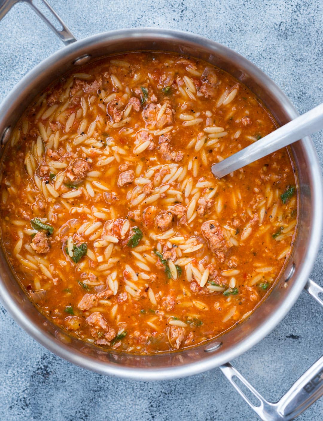 Orzo soup made with spicy Italian Sausage in a rich tomato flavor base in a pot.