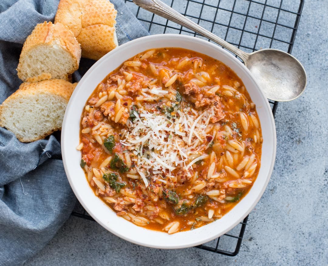 Orzo soup sprinkled with parmesan cheese served in a white bowl along with bread slices.