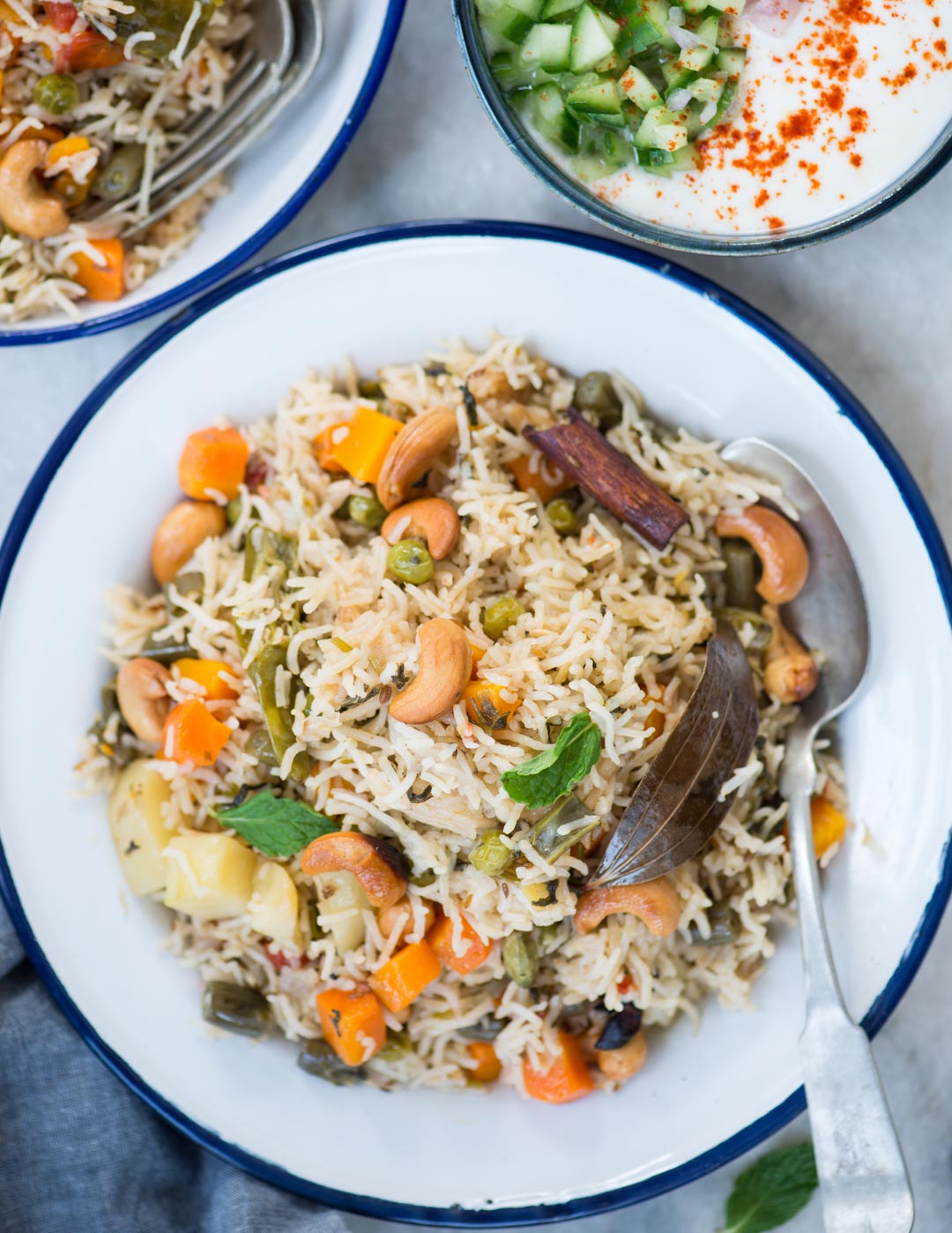 Veg Pulao with cashews, vegetables and whole spices in a white plate and spoon.