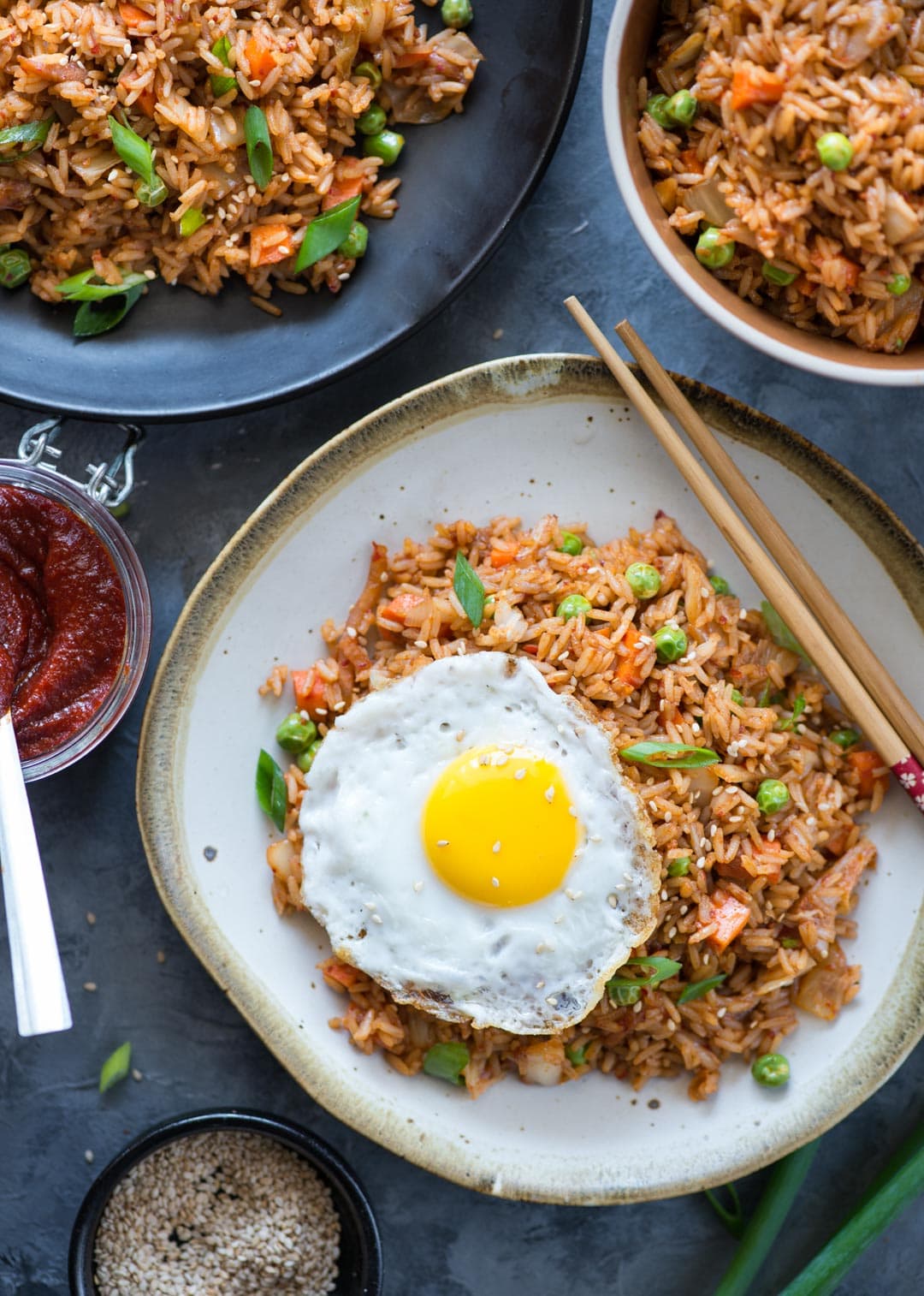 Quick and easy Kimchi Fried rice cooked and plated in a dark and white plate as well as in a bowl with a jar of gochujang and a sunny side up