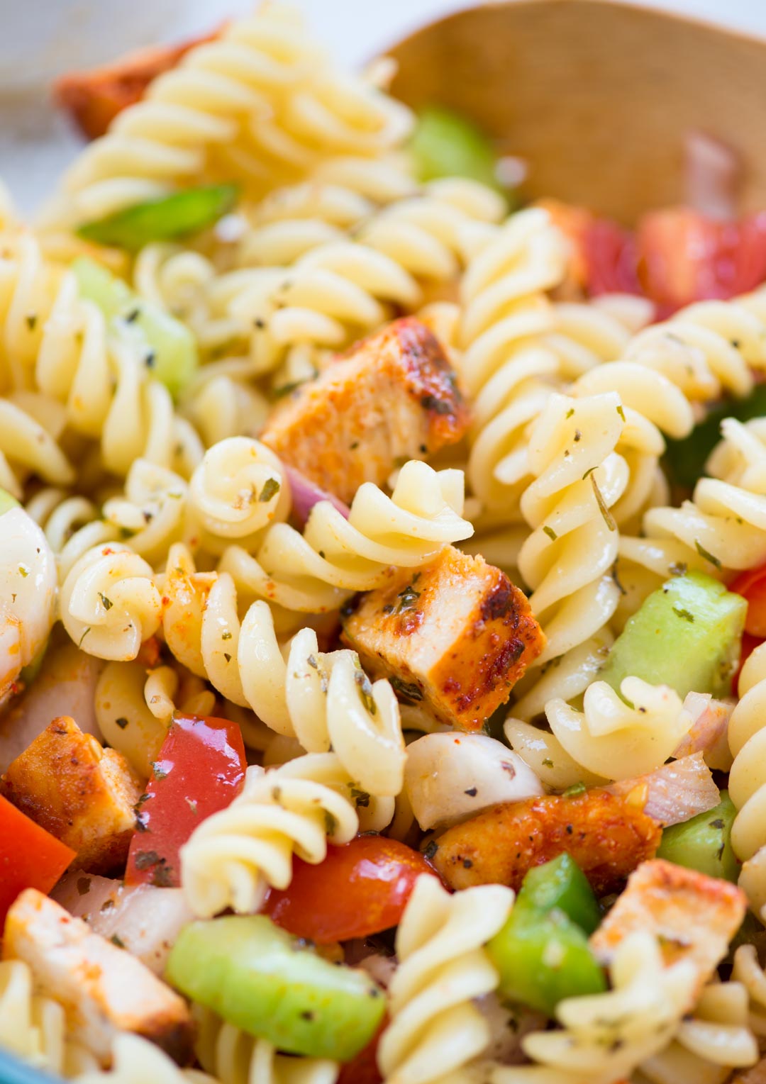 Close view showing chunks of grilled chicken, cooked fusilli pasta and bite-sized vegetables coated with lemon dressing.