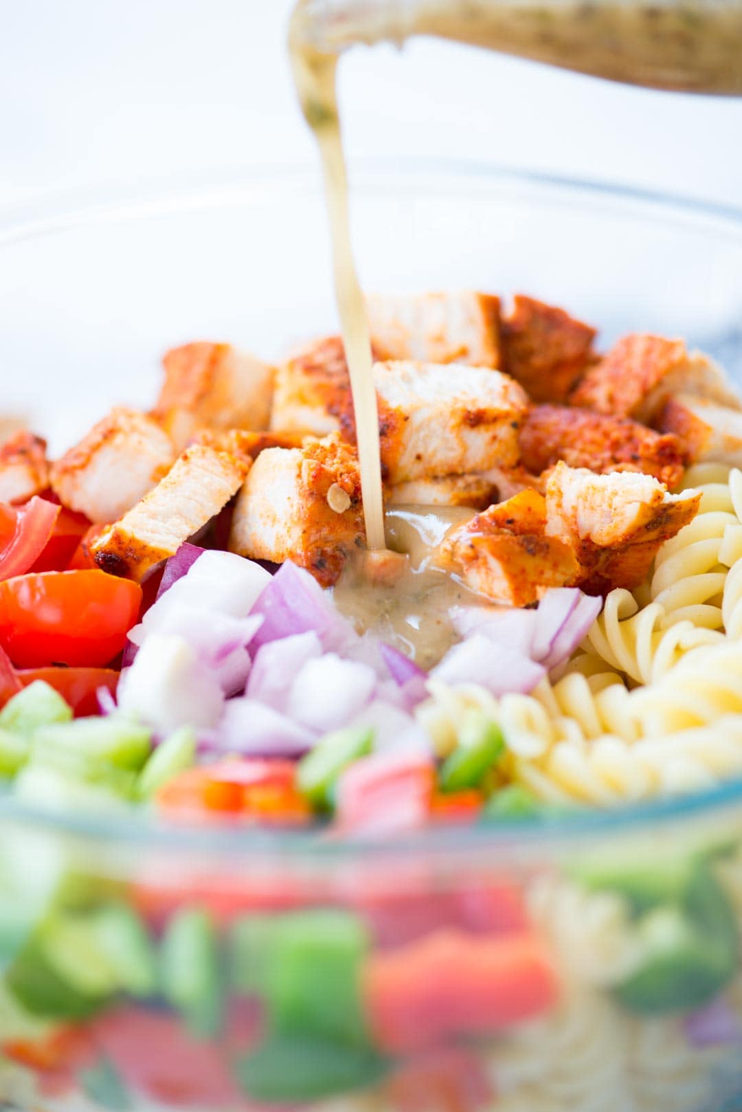 Lemon herb dressing poured on other ingredients of chicken pasta salad in a bowl.