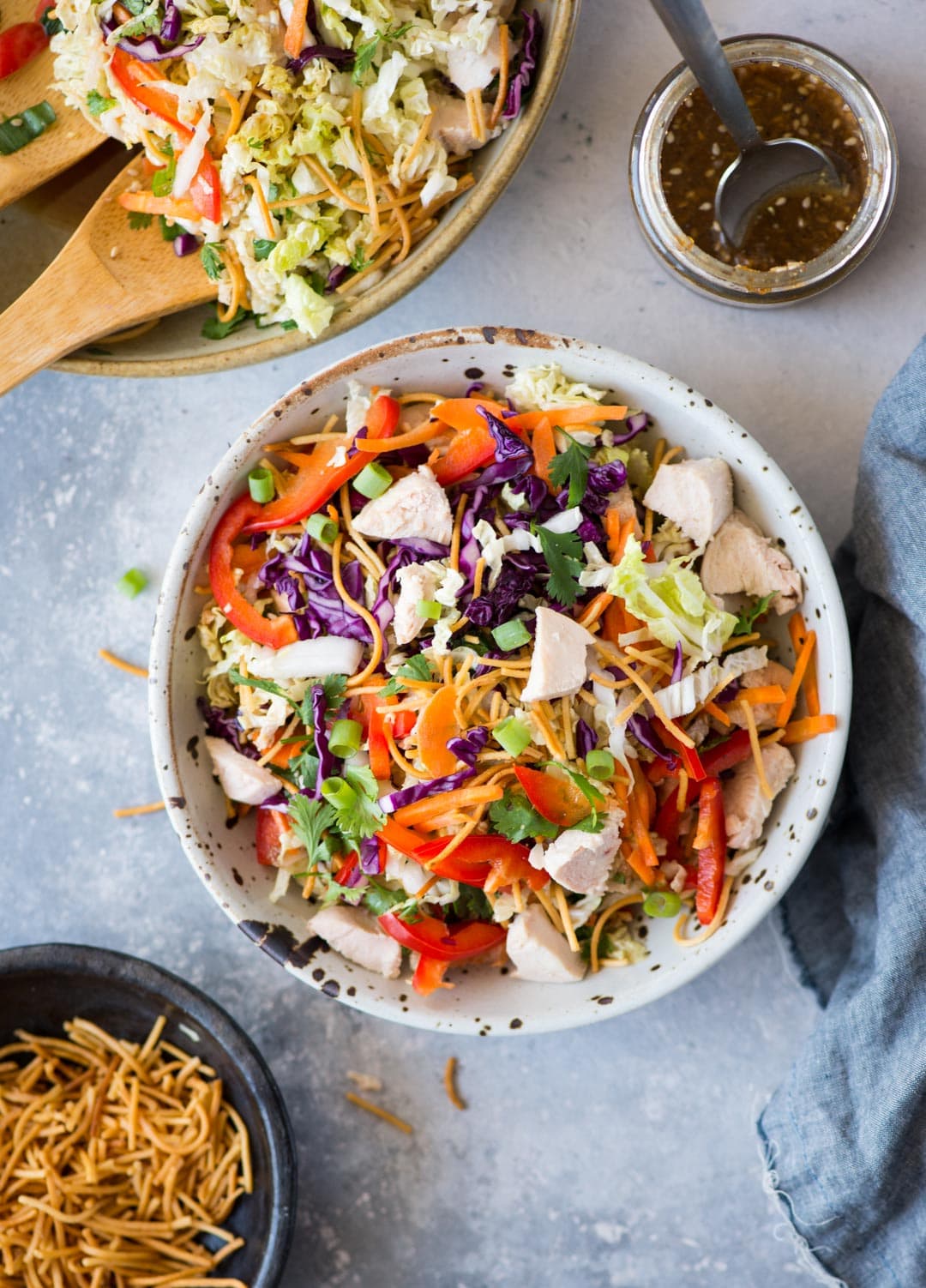 Top view of Chinese chicken salad served in a white spotted bowl with additional fried noodles on the side.