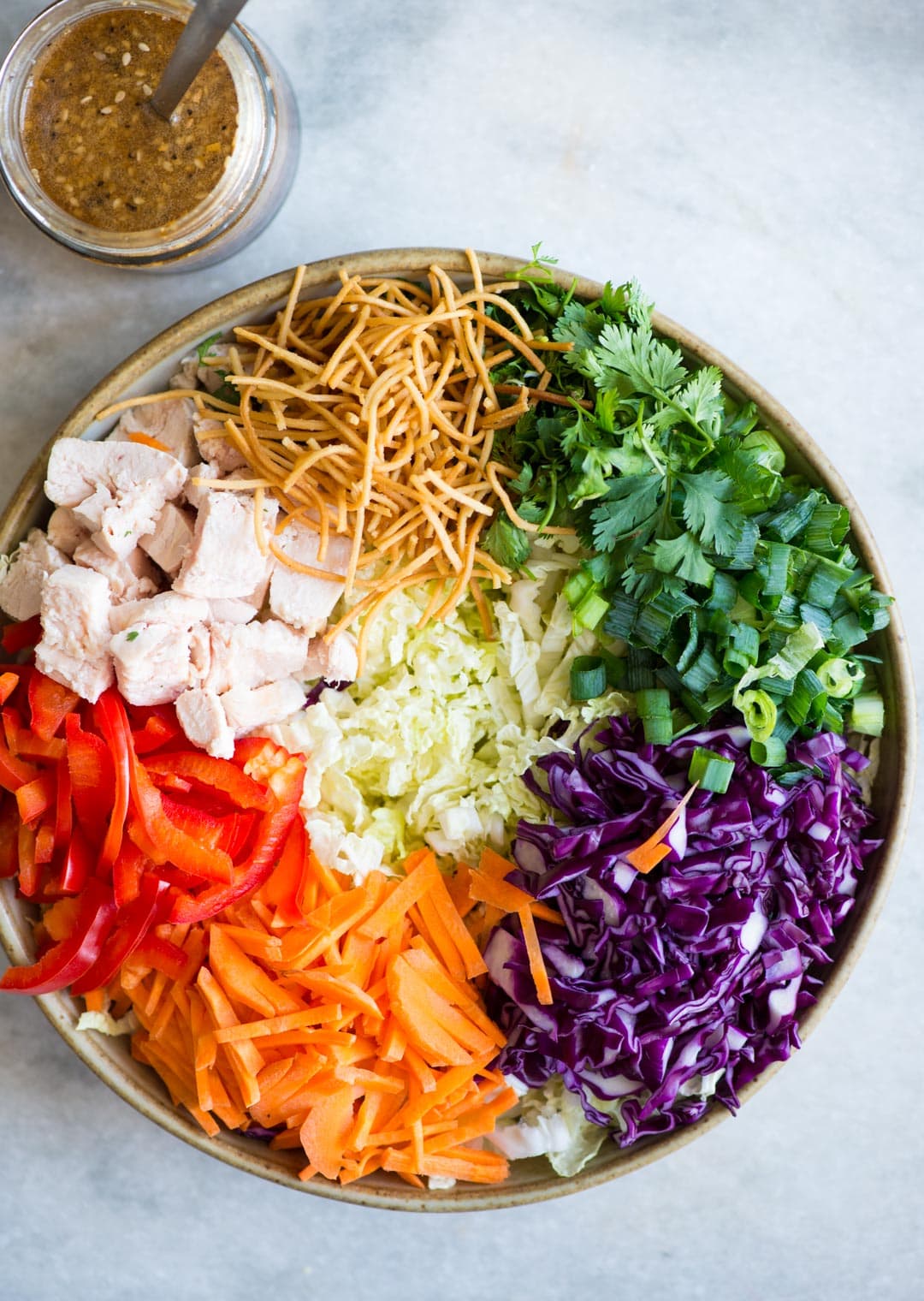 Ingredients to make asian or chinese chicken salad veggies like cabbage, carrot, peppers. juicy chicken, spring Onion, Crispy noodles, coriander and  a zest Asian dressing