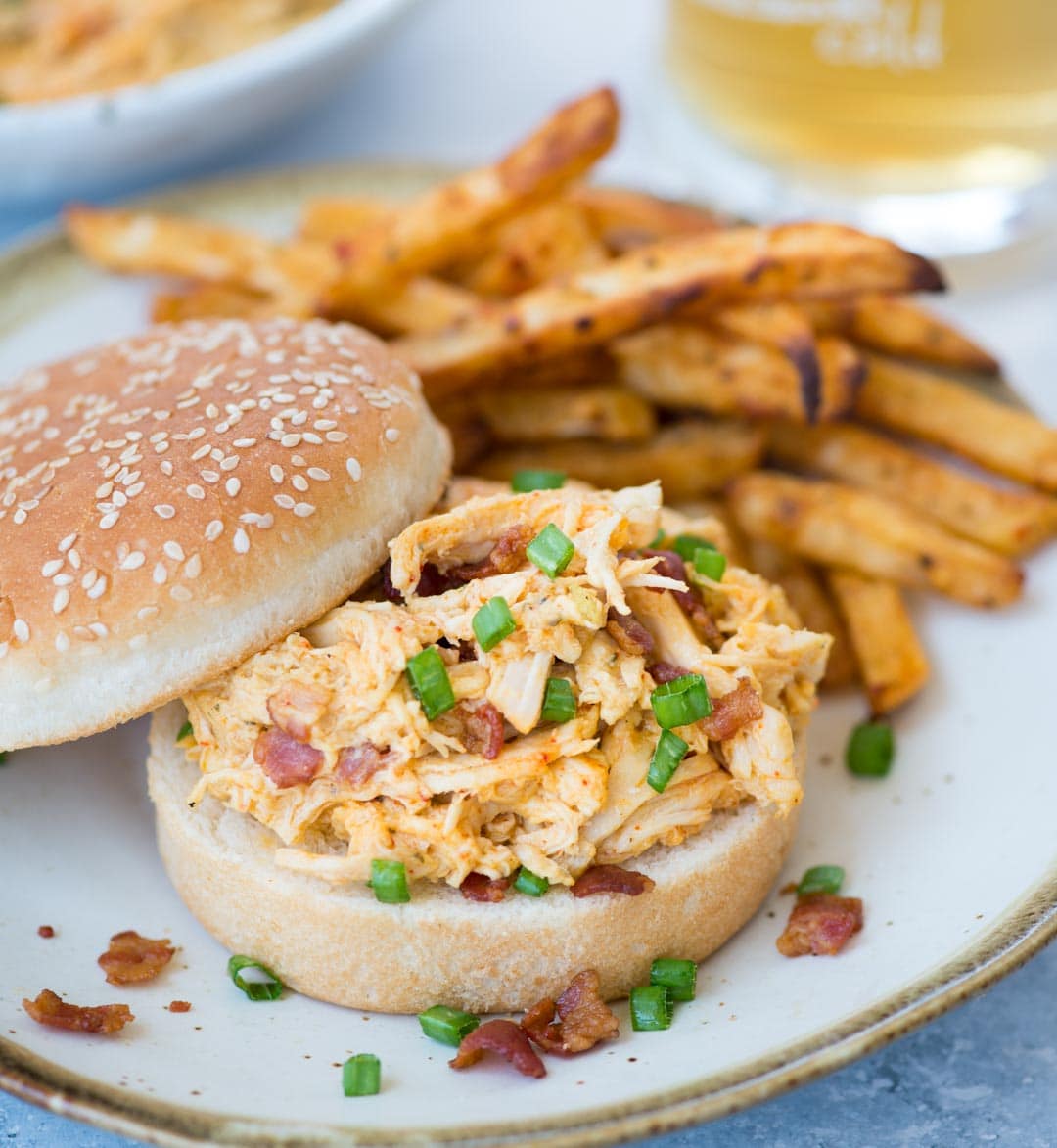 Close-up view of crack chicken with bits of bacon and green onion in a bun and is served with potato chips.