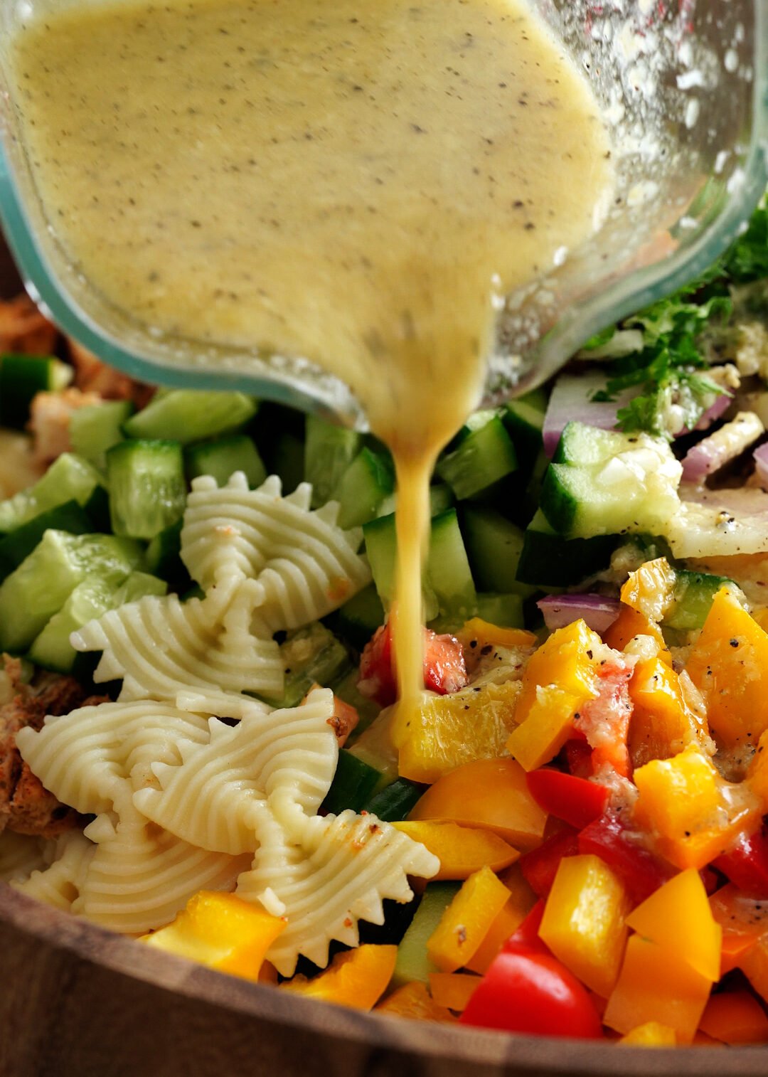 Lemon parmesan dressing pouring on pasta and chopped veggies. 