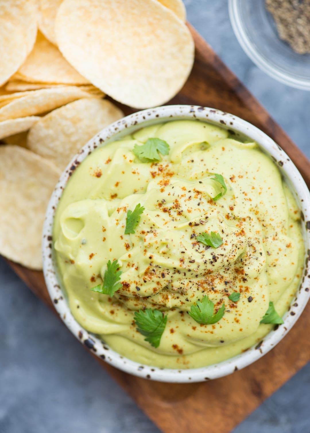 Creamy Avocado Dip shown in a small bowl, garnished with coriander leaves alongside potato chips