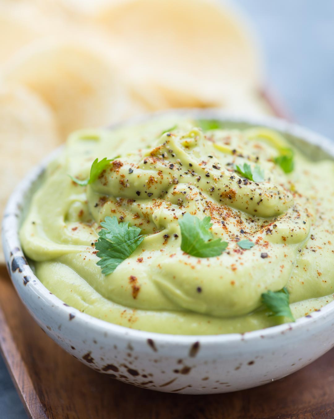 Close up image of creamy and soft avocado dip with cilantro leaves and chilli flakes as garnish on top.