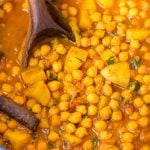 Close-up view of Chickpea curry with potato or also known as Chana Aloo, shown in a dutch oven and a ladle.