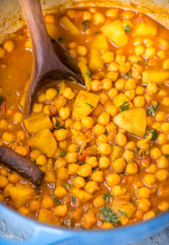 Close-up view of Chickpea curry with potato or also known as Chana Aloo, shown in a dutch oven and a ladle. 