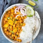 Chickpea curry with potato or Chana Aloo served in a bowl with rice, and slices of cucumber or onion.