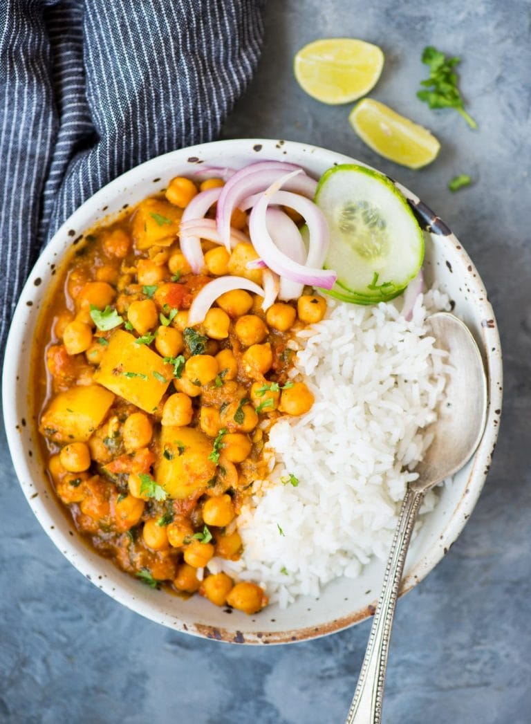 Chickpea curry with potato or Chana Aloo served in a bowl with rice, and slices of cucumber or onion.