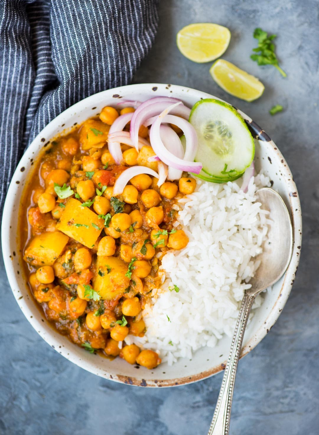 Chickpea curry with potato or Chana Aloo served in a bowl with rice, and slices of cucumber or onion.