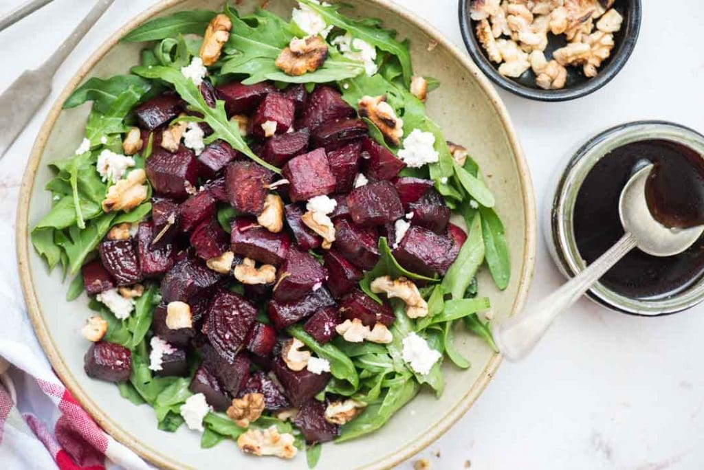 beetroot arugula salad in a bowl alongside balsamic dressing in a small bowl