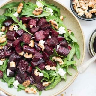 beetroot arugula salad in a bowl alongside balsamic dressing in a small bowl