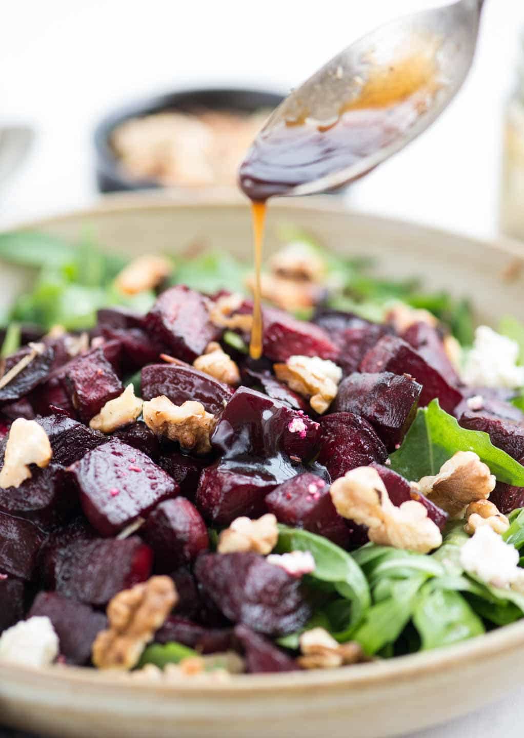 Closeup of Balsamic dressing poured over beetroot arugula salad with walnuts