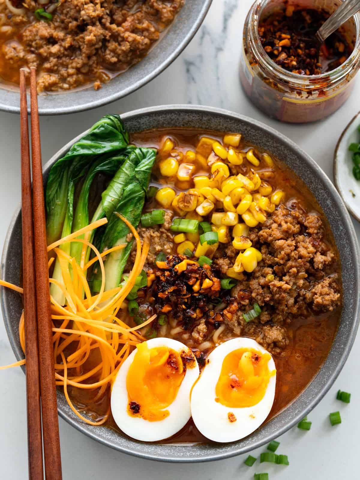 Bowl of ramen with spicy pork, soft boiled egg, bokchoy, sweetcorn, and chilli crisp topping.