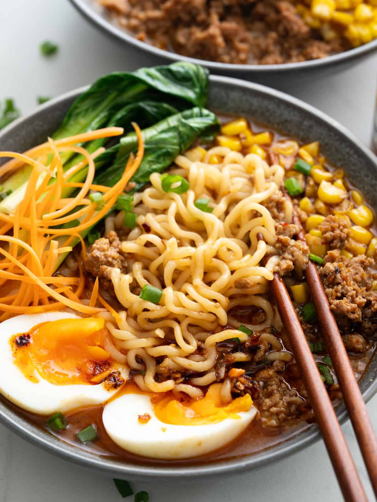 Bowl of ramen with spicy pork, soft boiled egg, bok choy, sett corn and chilli crisp topping