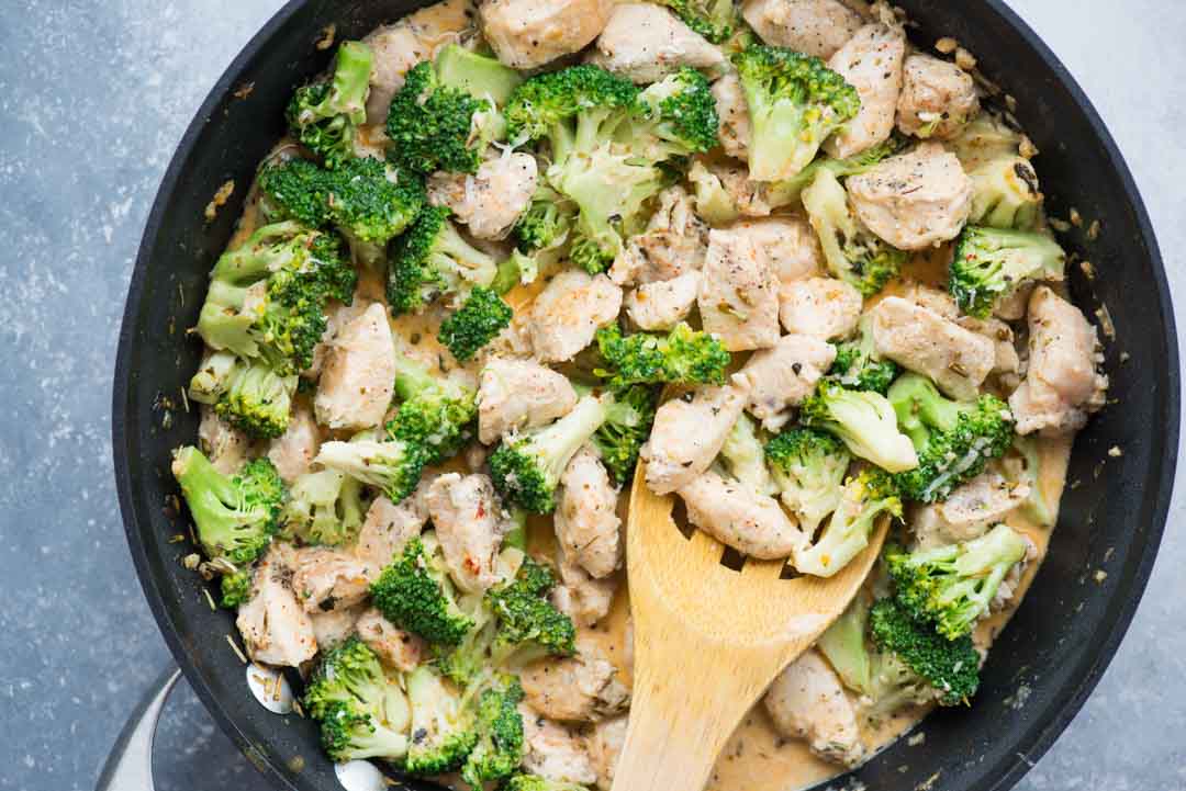 Cooked chicken and Broccoli stirred with a creamy and garlicky sauce in a black pan.