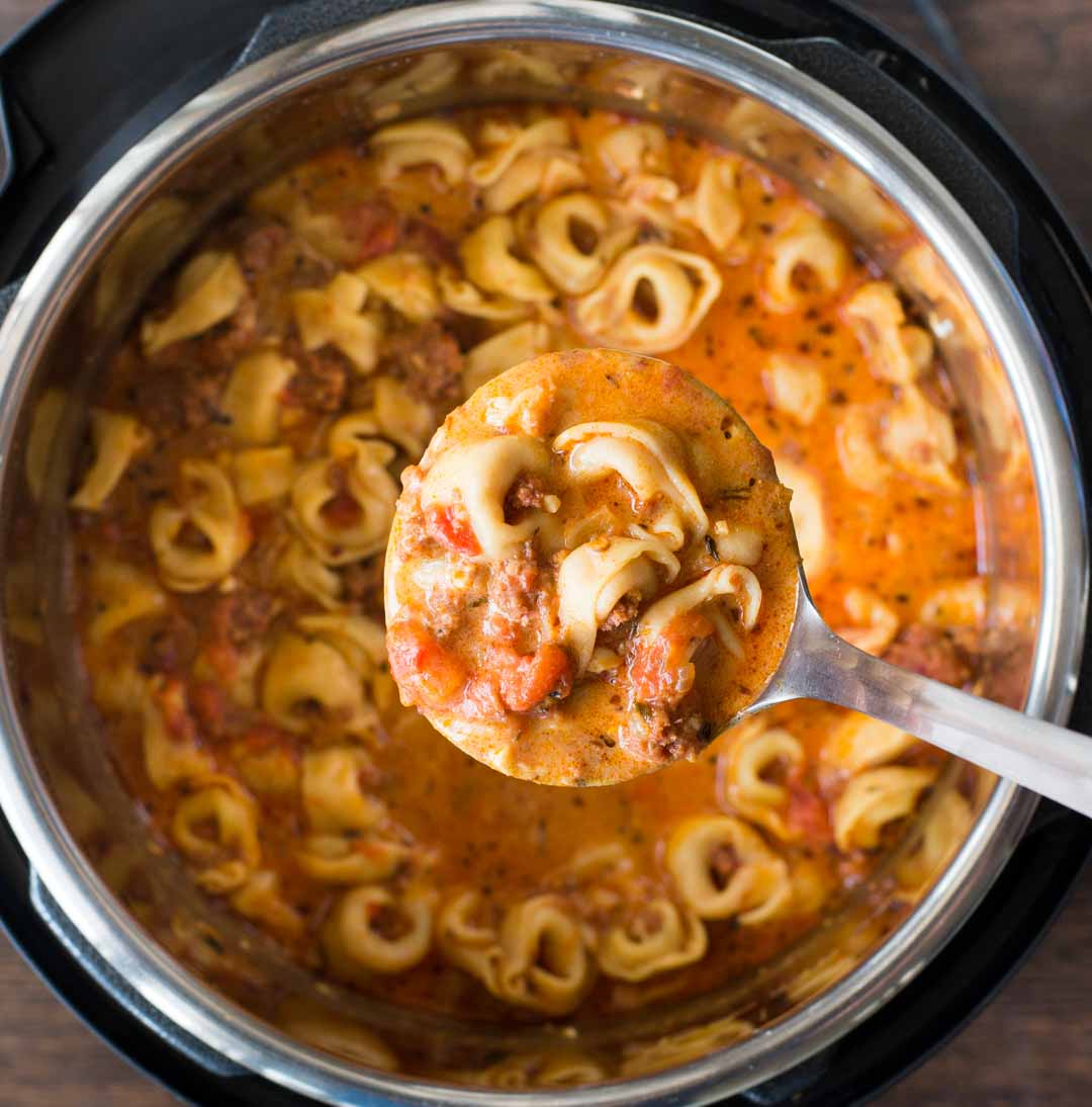 Rich and tomato-based tortellini Soup is picked up in a ladle from the instant pot.