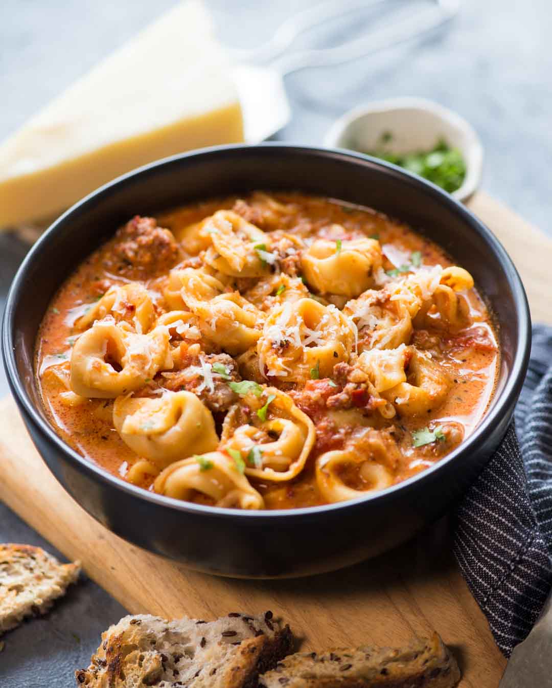 Winter favorite Cheesy Sausage Tortellini Soup is served in a black bowl with parmesan cheese sprinkled on it.