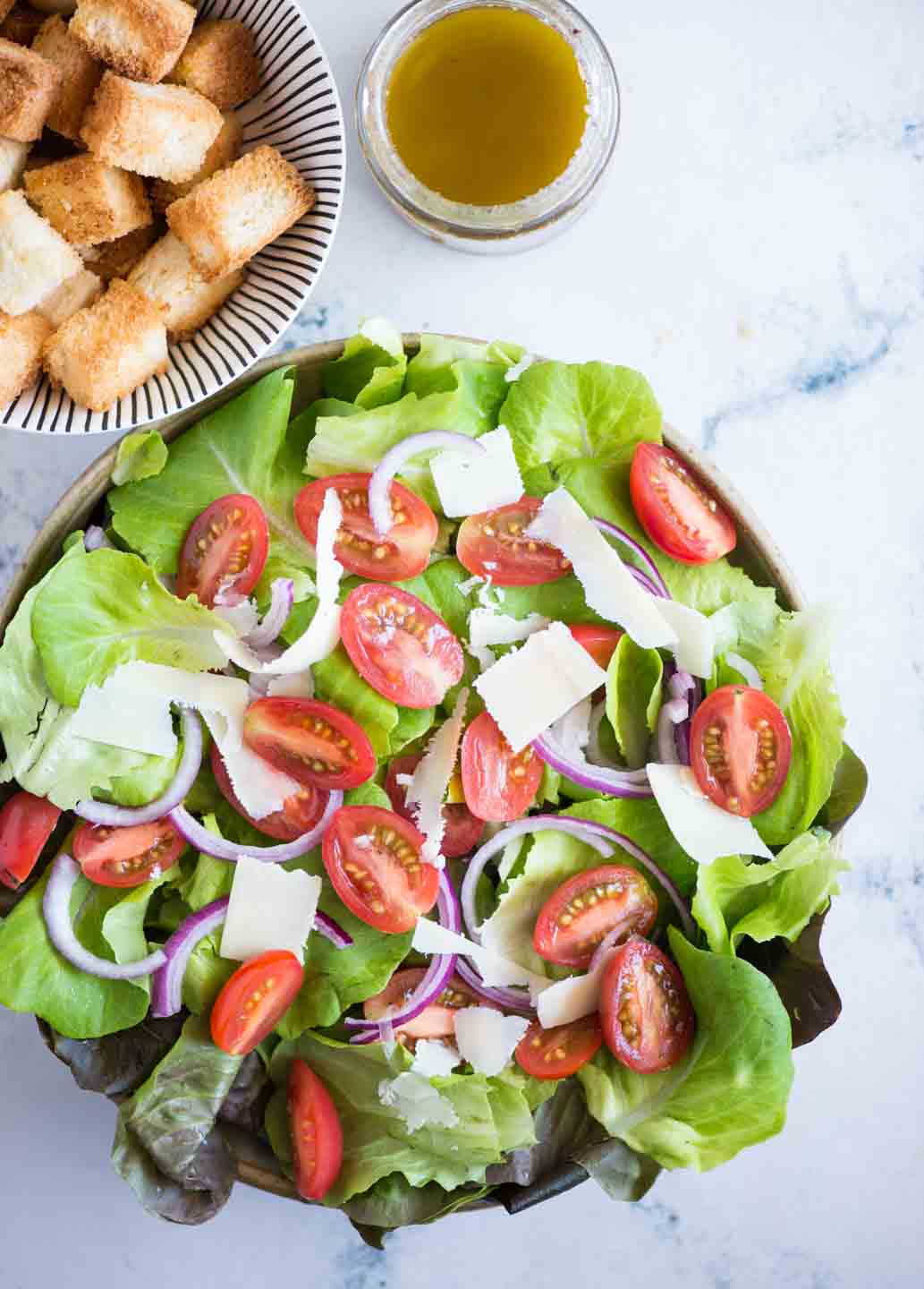 Top view of Italian Chopped Salad shows romain lettuce tossed with chopped cherry tomatoes, sliced onion and parmesan slices.