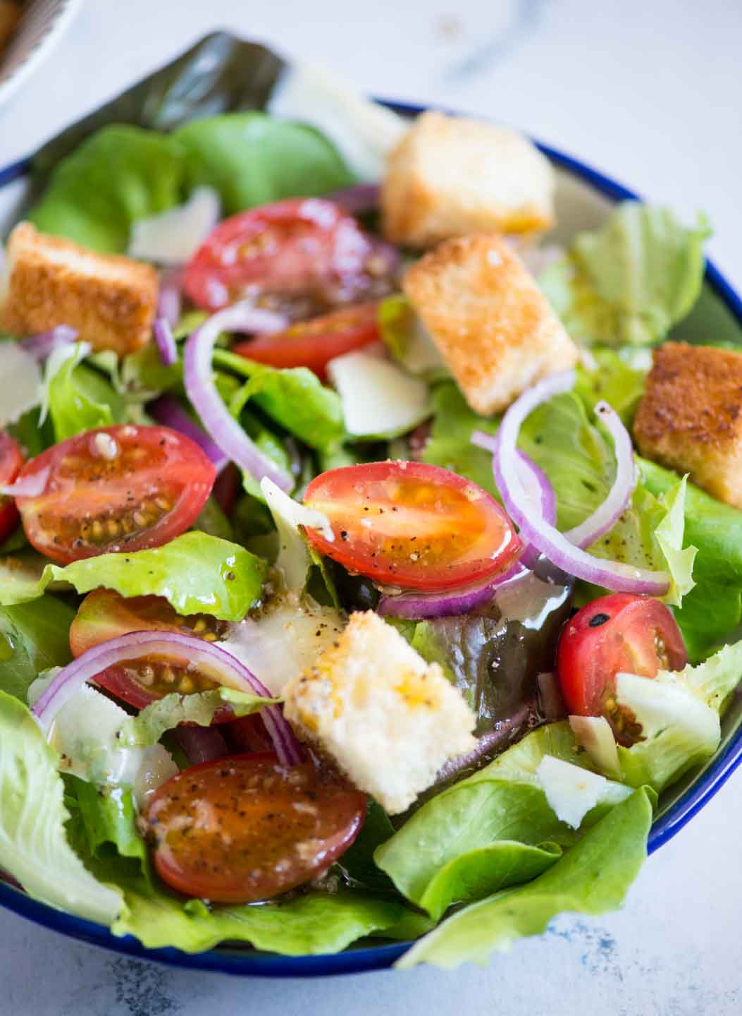 Close up view of Italian chopped salad with  croutons, cherry tomatoes, onion slices and romaine seen with a dressing.