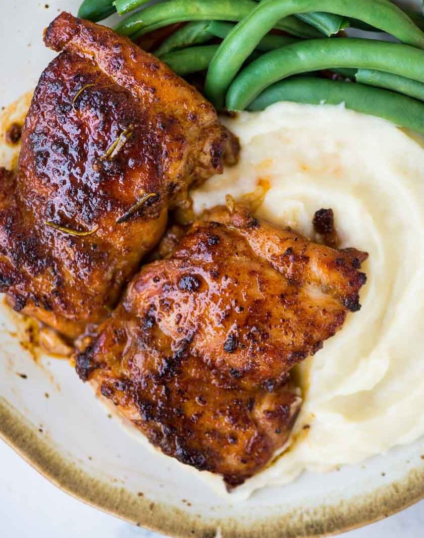 Chicken thigh with a seared crispy crust served on a bed of mashed potatoes and sauteed green beans