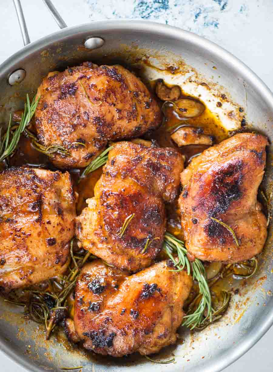 Image shows skinless boneless chicken thighs with a golden brown crust and black sear on surface and with a sweet-spicy sauce, cooked in a skillet.