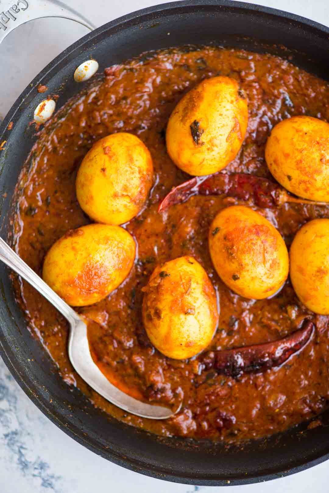 Picture of Egg Curry in a deliciously rich onion tomato gravy in a pan with a spoon.