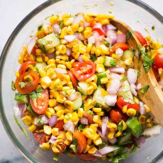 Ingredients for roasted corn salad tossed around in a big bowl with a spoon.