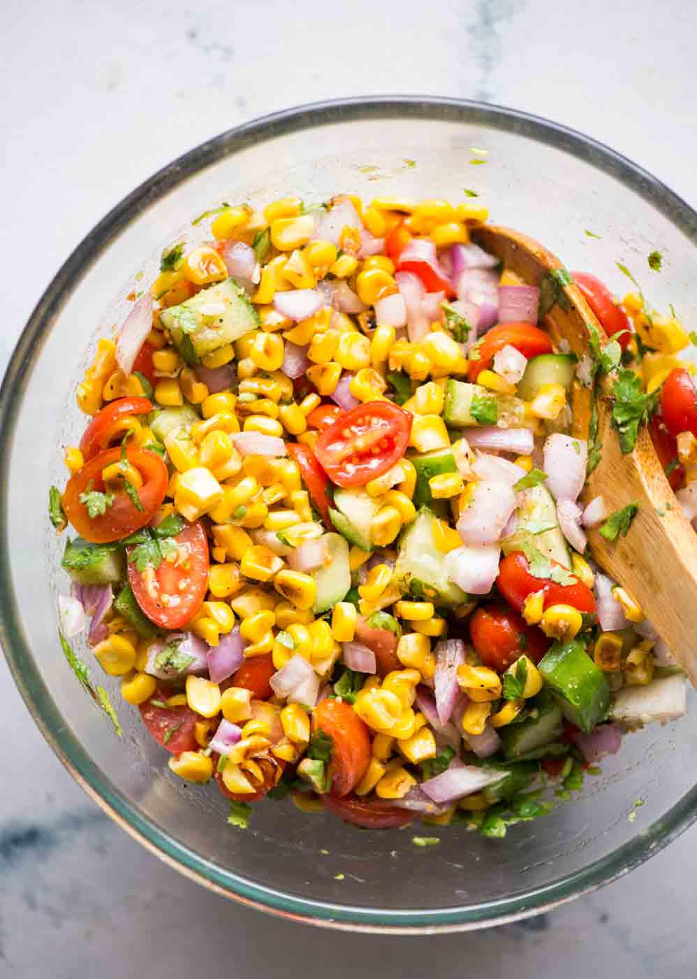 Ingredients for roasted corn salad tossed around in a big bowl with a spoon.