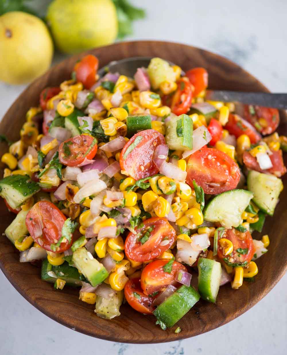 Salad made of roasted corn and chopped veggies with a tangy dressing served in a wooden bowl.