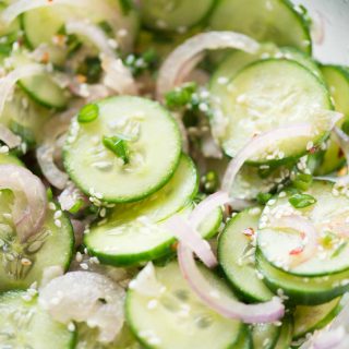 Close view of cucumber salad shows sliced cucumbers, onions, green onions mixed with sesame seeds.