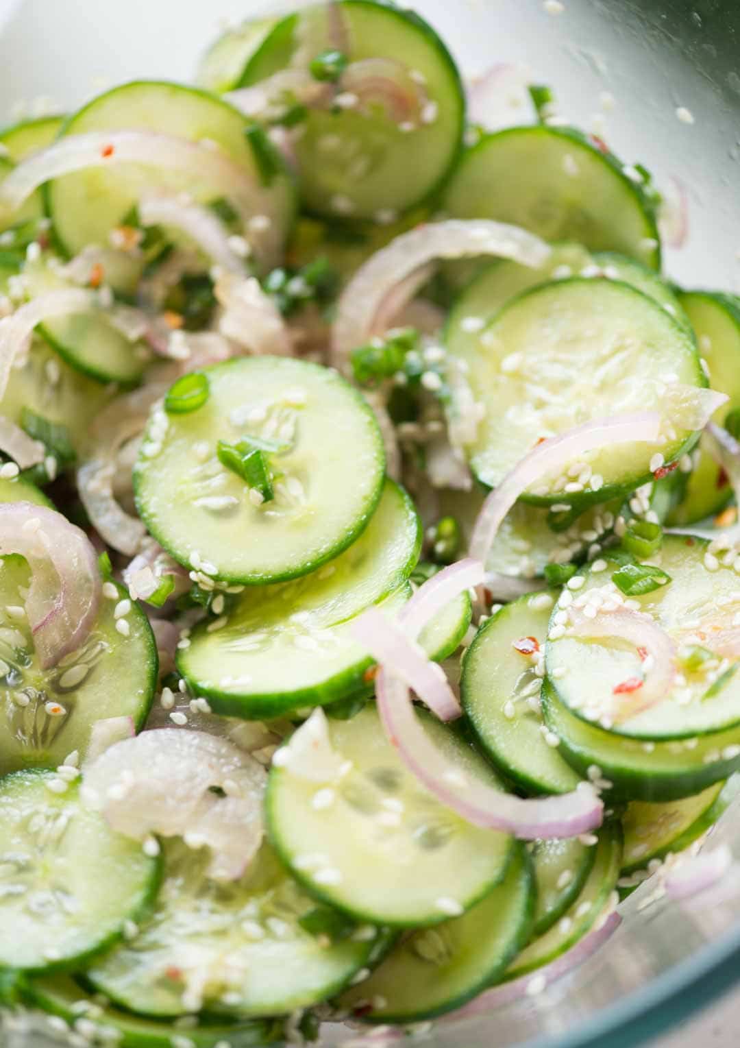 Close view of cucumber salad shows sliced cucumbers, onions, green onions mixed with sesame seeds.